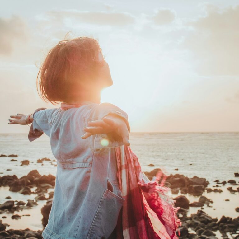a woman standing on a rocky beach with her arms out