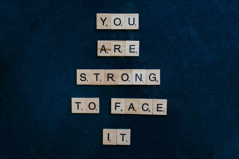 Scrabble tiles spelling 'You Are Strong To Face It' on a dark surface, conveying courage