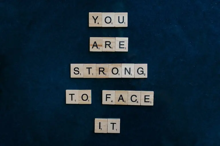 Scrabble tiles spelling 'You Are Strong To Face It' on a dark surface, conveying courage